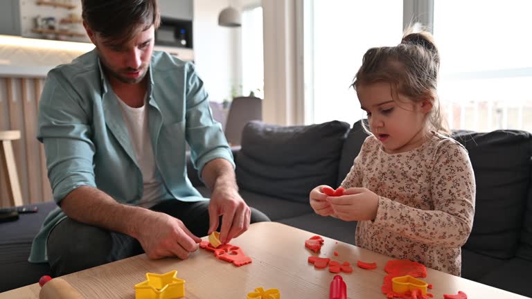 Parents playing with daughter at home with clay. Family with one little girl moulding shapes in play clay