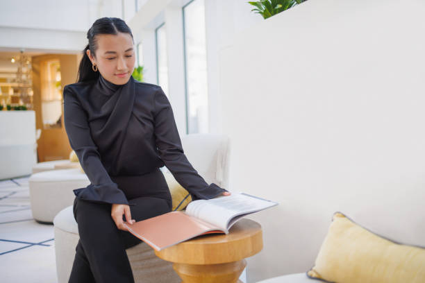 istock Young Asian woman working from remote location in hotel lobby, going through figures in a report 2015658874