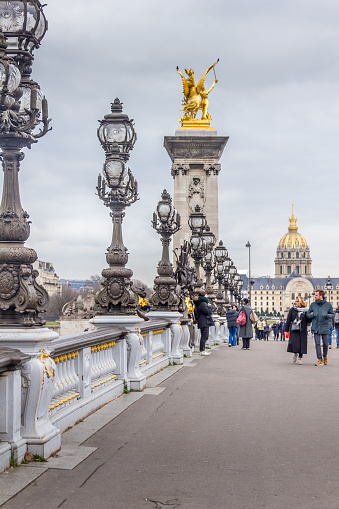 Paris, France - 5 March, 2023: People walking in the Alexandre III bridge. The traditional attraction is known as the most ornate, extravagant bridge in the city.