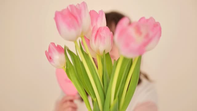 Mothers Day. daughter gives her mother a bouquet of pink tulips and a pink heart on a beige background.Postcard for mom.