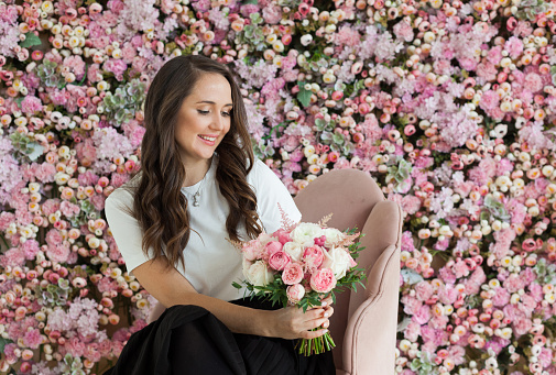 Young healthy woman smiling and holding colorful pink color flower bouquet on floral spring or summer background, studio fashion beauty portrait