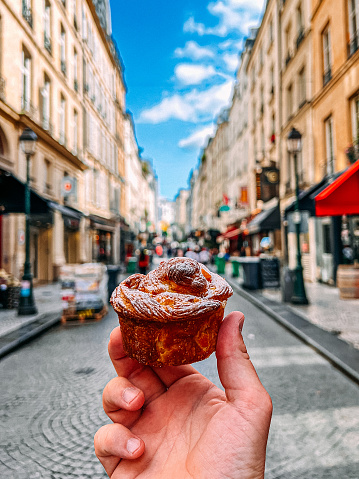 Young Man's Hand Holding a Kouign Amann Pastry in 2nd Arrondissement, Paris on a Sunny Summer Day