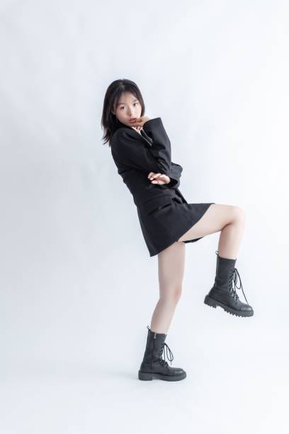 Asian woman in black suit and boots posing on white background