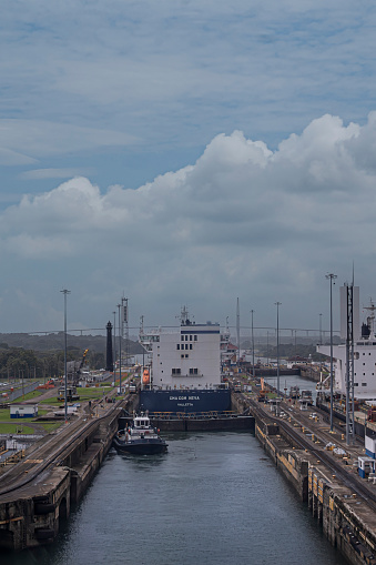 Panama Canal, Panama - July 24, 2023: Entering Gatun locks on Atlantic side of canal under blue cloudscape. CMA CGM container ship inside. Atlantic bridge on horizon. Historic lightower
