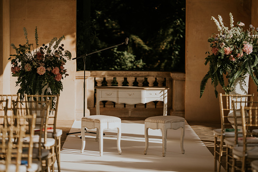 wedding ceremony altar. Table and two small chairs. two floral centers on the sides. There are several chairs with gold color.