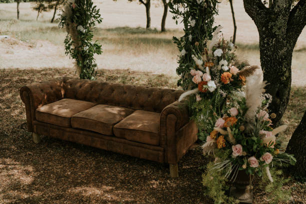 Detailed plan of an altar for a rustic ceremony held in a natural setting. We see a sofa with an arch made of flowers and plants. Next to the leather sofa, a large bouquet of pink roses and pampas feathers.