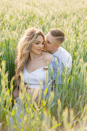 A man plants a kiss on the womans cheek, surrounded by tall grass in a natural landscape. They smile, their hands intertwined, happy and at peace in nature