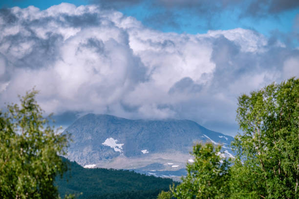 Scenic zoomed view at heavy blue clouds above remote mountain in in Norwegian Mountains range. Blurry trees at foreground at sides of photo. Sweden, Lapland, Joesjo