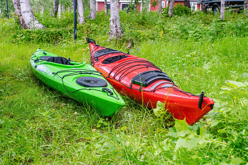 Two kayaks - red and green ones are on the green grass, close up low level side photo