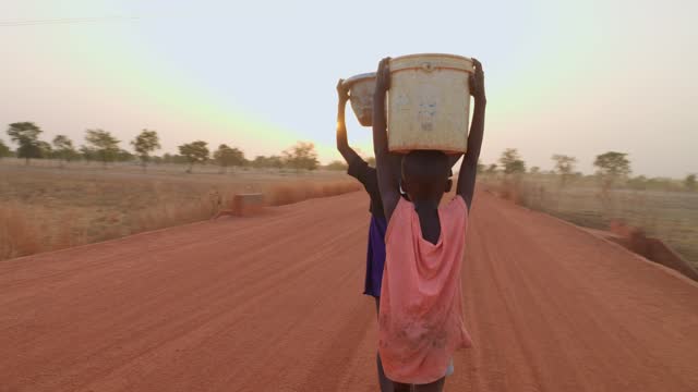 black african young cute little child carrying purified water over their head in remote rural african village at sunset