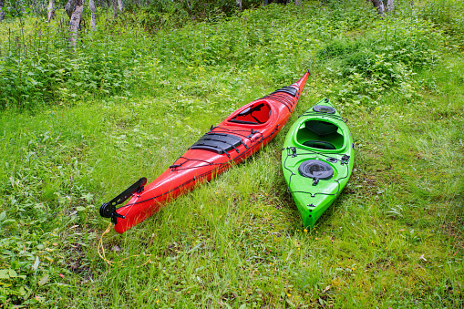 Two kayaks - red and green ones are on the green grass
