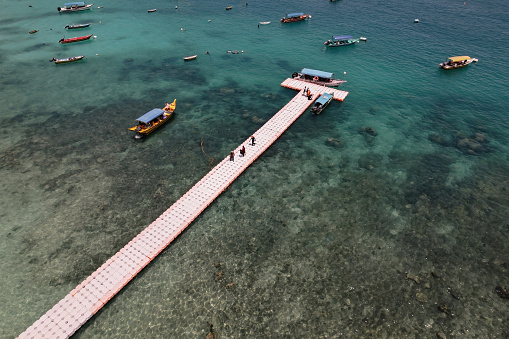 An Aerial view of natural clear blue sea with a floating sea bridge and boat, Perhentian Kecil Island.