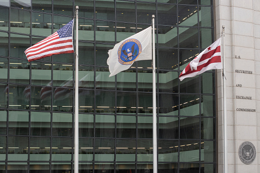 Washington, DC, USA - Jun 23, 2022: Waving flags of the United States, the SEC, and Washington, D.C. are seen in front of the U.S. Securities and Exchange Commission (SEC) headquarters building.