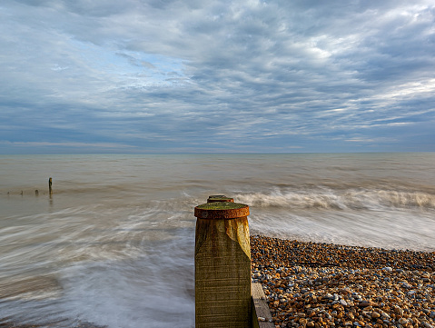 Waves roll into the shingle beach at Pett Level in East Sussex. The day is cloudy, but the late afternoon sun is breaking through adding some interesting light.