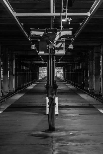 Black and white image of a vast, snow-covered railway yard featuring numerous tracks, tall electric poles, a small shed, and distant apartment blocks, conveying cold, industrial urban infrastructure.