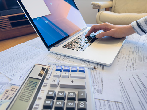 Close up photo of a woman doing taxes with laptop and tax forms in a house