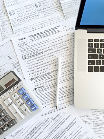 Close up photo of a woman doing taxes with laptop and tax forms in a house