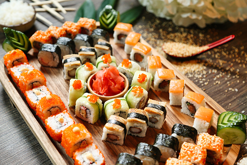 A wooden tray filled with a variety of delicious sushi rolls, including salmon, tuna, California, and spicy tuna.