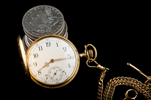 Antique pocket watch from 1917 with old U.S silver dollars on black background.