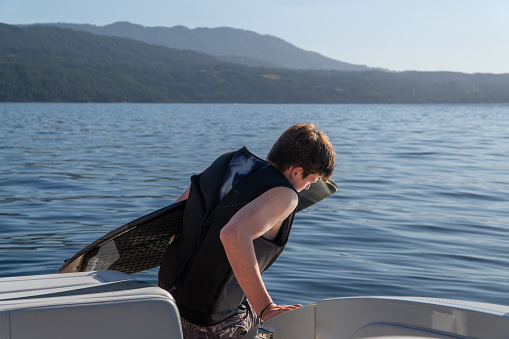 A young man getting into the water with his wakeboard to wakesurf on the lake.