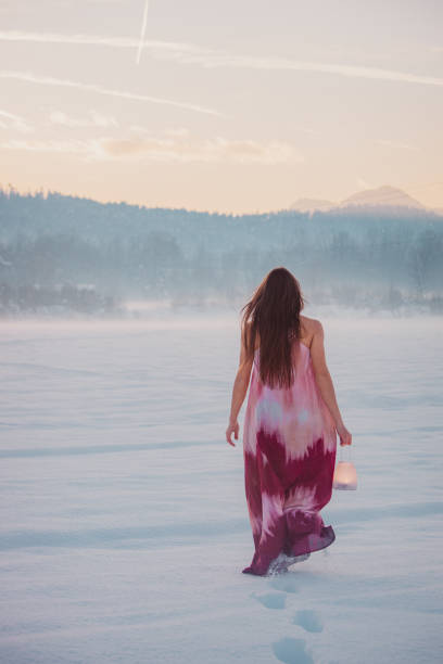 Young woman wearing long dress explores winter landscape with lantern