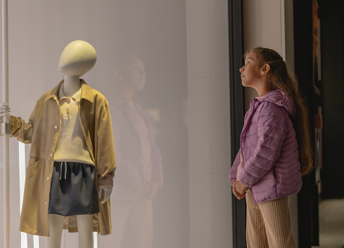 Girl outside a store looking through the windows at a mannequin