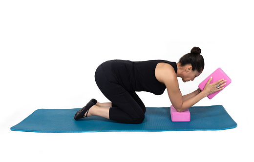 Specialized trauma yoga and Pilates exercises for elderly people on the mat, middle woman trainer posing with two pink bricks for exercises. In the studio isolated on white.