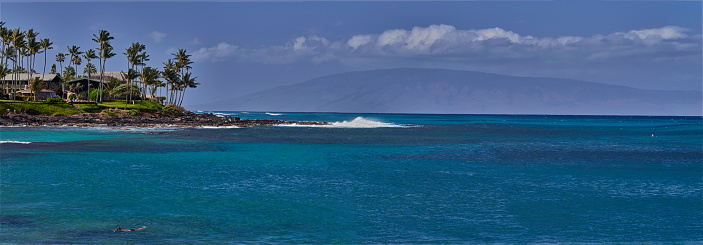 swimmer and distant surfer, enjoying napili bays warm water, with the island of lanai, rising out of the pacific in the background.