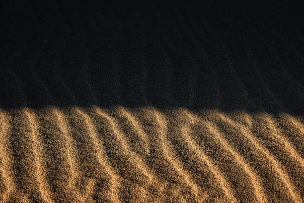 Full frame texture of sunrise casting shadows over smooth shaped golden desert sand dunes in Western Australia.