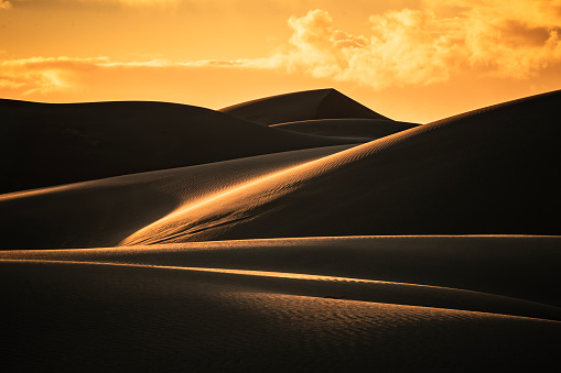 The small figure of a man walks in the distance across a desert towards towering sand dunes leaving a trail of distinct footprints behind - Great Sand Dunes National Park, Colorado - USA