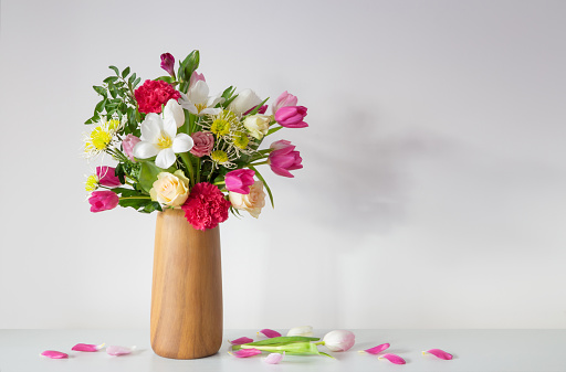 beautiful flowers  in vase on shelf  on background white wall