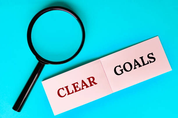 istock Top view of magnifying glass and notepad with Clear Goals text on light blue background 2016409933