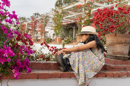 Little latin girl with straw hat and dress in a flower standing garden