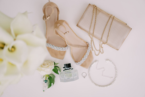 Wedding ring lies on a white table near the bride shoes, handbag and perfume. Top view. High quality photo