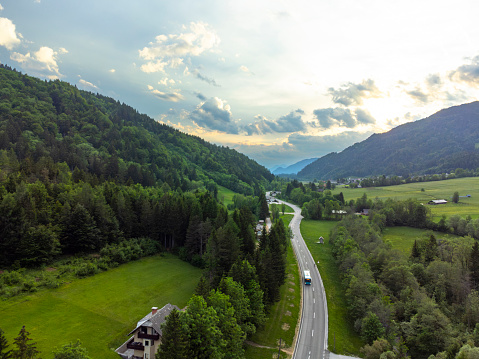Aerial view of a scenic road winding through lush green countryside with mountains in the background.
