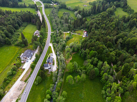 Aerial view of a winding road through lush green countryside with trees and buildings.