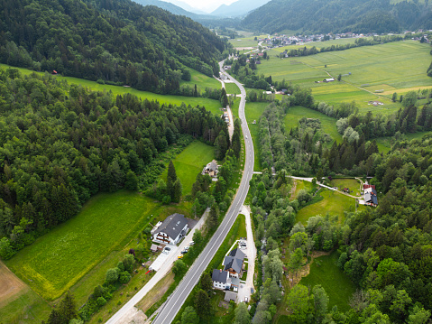 Aerial view of a winding road through lush green countryside with trees and buildings.