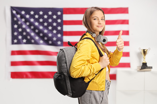 American teen student with headphones and backpack gesturing thumbs up