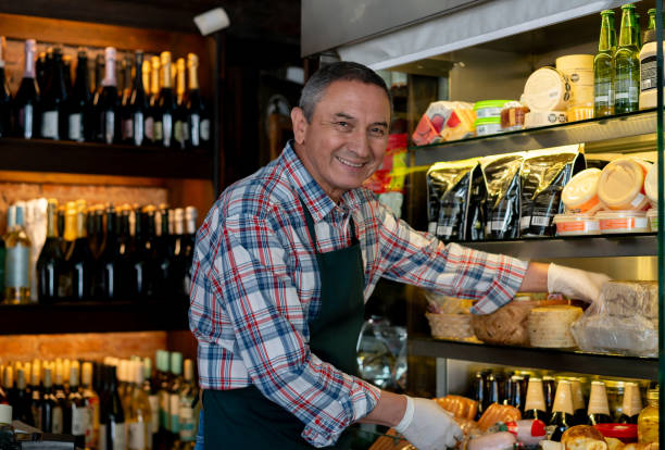 istock Senior man working at a charcuterie arranging the refrigerated display while smiling at the camera 2016551572