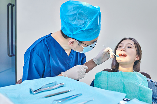Asian dentist examining teeth to young female patient in dental's clinic.