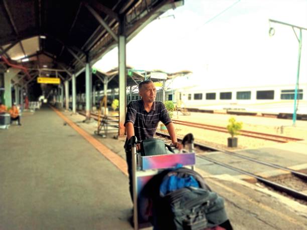 Asian man is waiting for the train with his luggage cart.