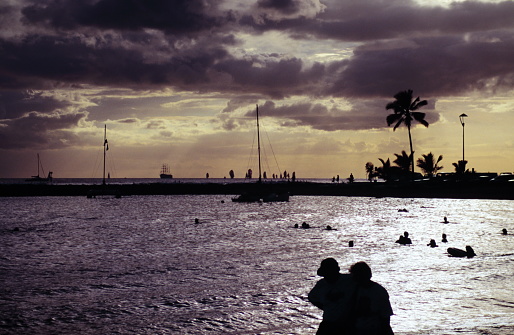 The silhouette of Tourists enjoying at Waikiki Beach, Honolulu, Oahu, Hawaii against sunset in early 1990s