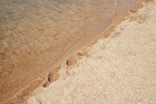 clear water and brown sand of the Sabyndykol mountain lake in Bayanaul National Park. diagonal line and texture background. high tide, sandy beach on sun day, vacation concept. top view