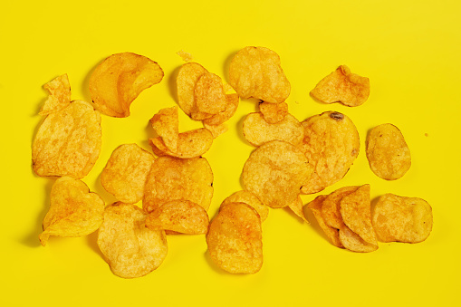A group of golden potato chips on a yellow background. Unhealthy food concept