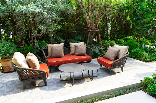 Backyard outdoor patio with modern red wicker sofa and pillow surround with lush green tree.