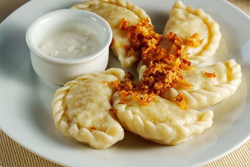 White plate showcases an array of delectable dumplings, perfectly paired with a luscious bowl of flavorful dip.