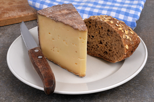 Piece of tomme des Pyrénées on a plate with a piece of bread and a knife close-up