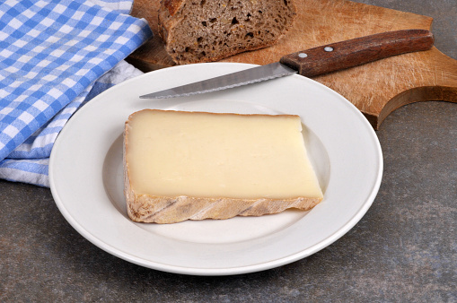 Piece of sheep tomme on a plate with a knife close-up