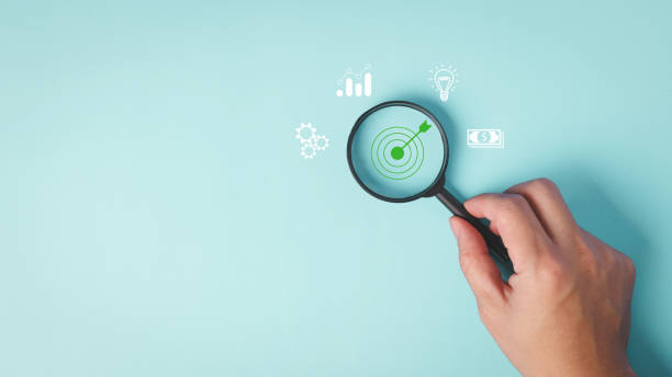 istock A hand holding a magnifying glass focuses on a target symbol, 2017044503