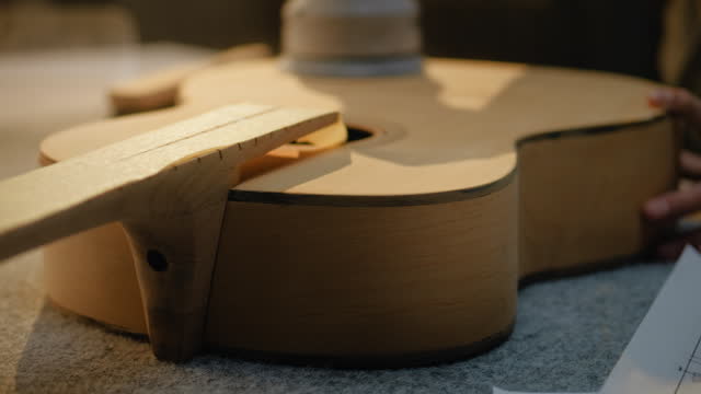 Close up of craftsman grinding guitar body using grinding machine